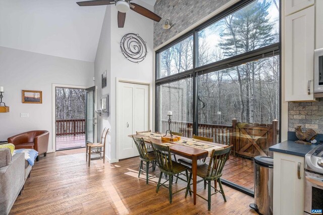 dining area featuring baseboards, ceiling fan, high vaulted ceiling, and wood finished floors