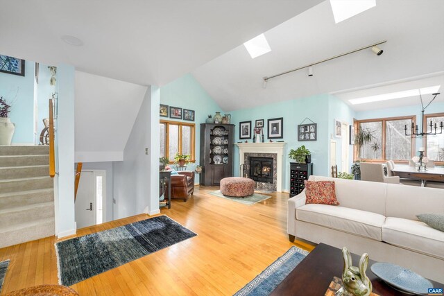 living room with rail lighting, stairway, a high end fireplace, wood finished floors, and vaulted ceiling with skylight