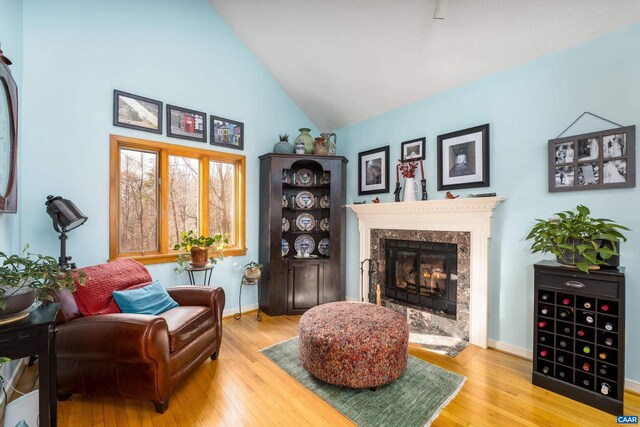 living area with high vaulted ceiling, wood finished floors, a high end fireplace, and baseboards