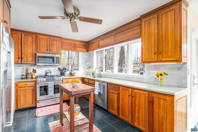 kitchen with appliances with stainless steel finishes, brown cabinets, a wealth of natural light, and dark tile patterned flooring