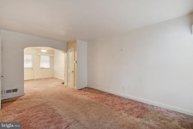 carpeted empty room with arched walkways, a ceiling fan, visible vents, and baseboards