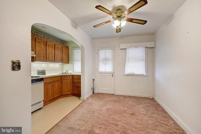 kitchen featuring under cabinet range hood, light carpet, a sink, white gas range oven, and brown cabinetry