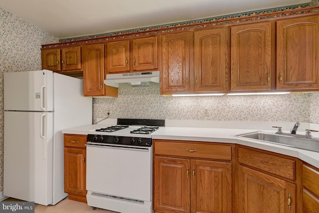 kitchen with brown cabinets, under cabinet range hood, white appliances, and a sink