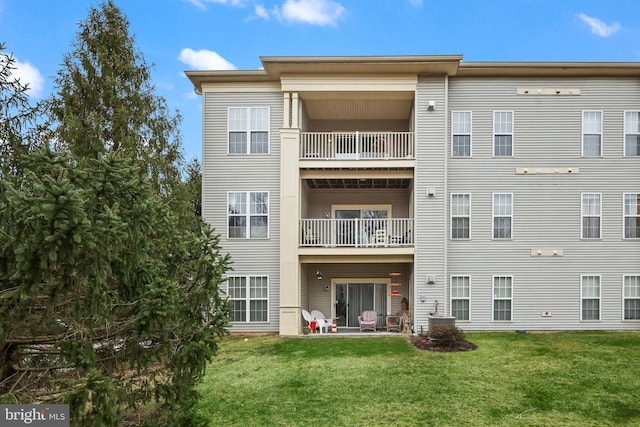 rear view of property featuring a lawn, a balcony, and a patio