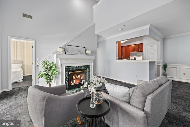 living room featuring visible vents, dark colored carpet, crown molding, a fireplace, and a decorative wall