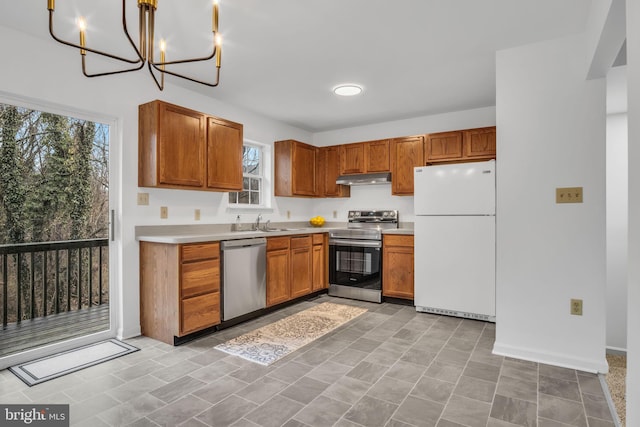 kitchen with light countertops, appliances with stainless steel finishes, brown cabinetry, a sink, and under cabinet range hood