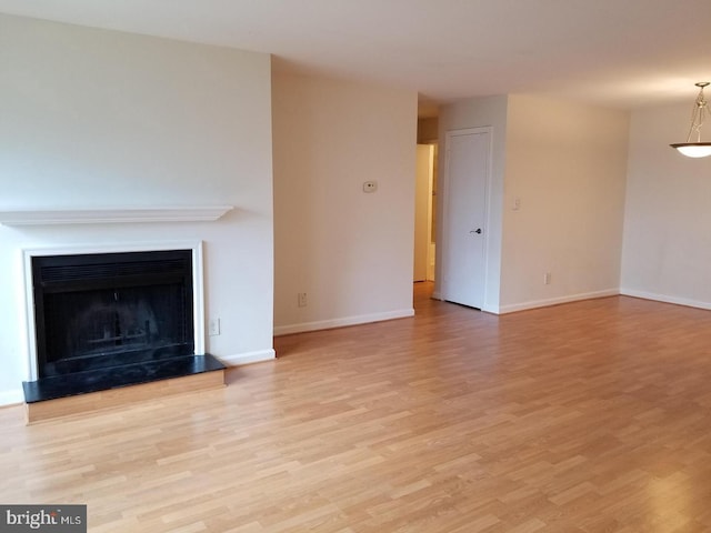 unfurnished living room with light wood-type flooring, baseboards, and a fireplace with raised hearth