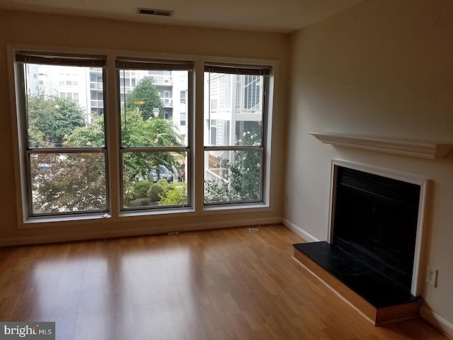 unfurnished living room featuring baseboards, visible vents, a fireplace with raised hearth, and wood finished floors