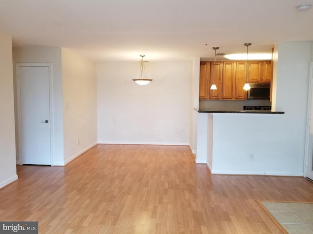 kitchen featuring baseboards, dark countertops, stainless steel microwave, decorative light fixtures, and light wood-type flooring