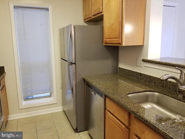 kitchen with dishwasher, light tile patterned flooring, a sink, and dark stone countertops