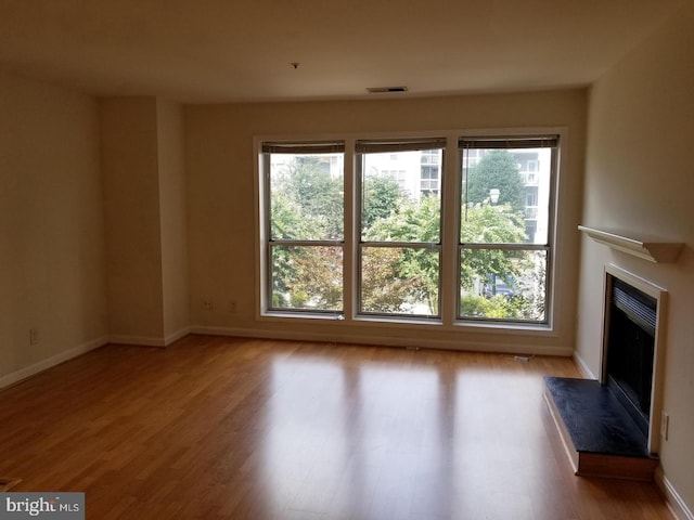 unfurnished living room featuring baseboards, visible vents, a premium fireplace, and wood finished floors