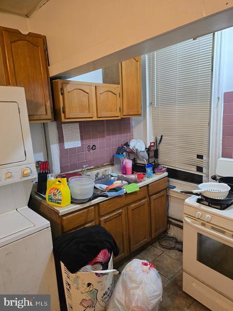 kitchen featuring brown cabinets, gas range gas stove, stacked washer and dryer, tasteful backsplash, and tile patterned flooring