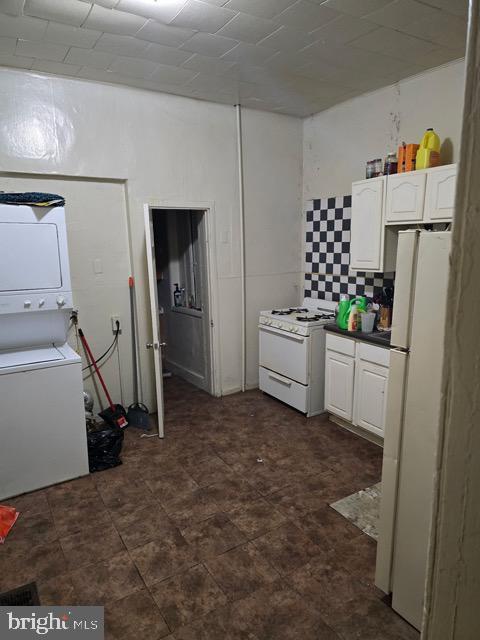 kitchen featuring white appliances, stacked washing maching and dryer, white cabinets, and decorative backsplash