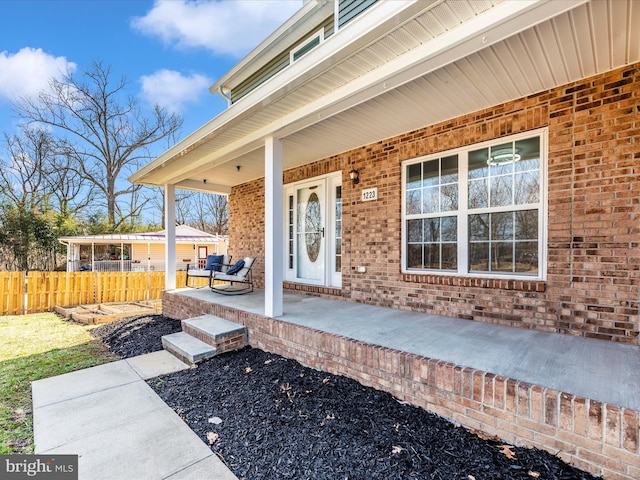 view of exterior entry with brick siding, fence, and covered porch