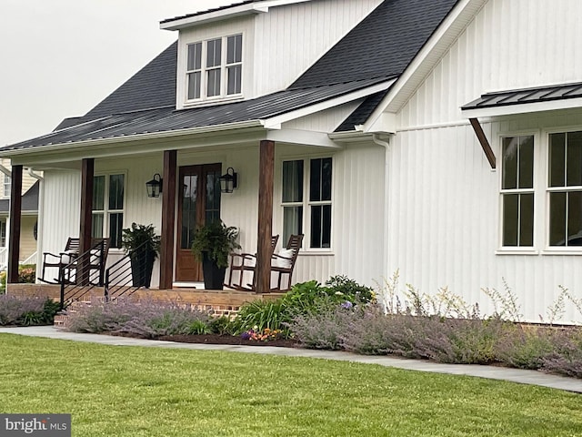 entrance to property with a porch, roof with shingles, metal roof, a yard, and a standing seam roof