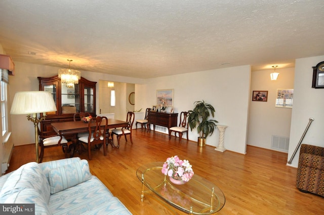 living area with visible vents, light wood-style flooring, a textured ceiling, and an inviting chandelier