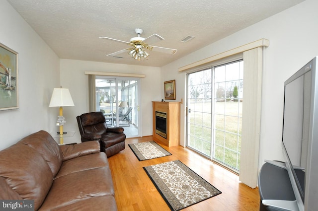 living room with light wood-style floors, plenty of natural light, and a glass covered fireplace