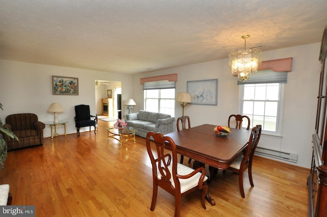 dining area with light wood finished floors, a baseboard radiator, plenty of natural light, and a notable chandelier