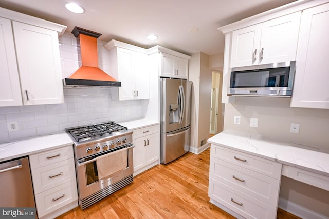 622 Hastings Rd, Baltimore, MD 21286 - kitchen featuring stainless steel appliances, wall chimney exhaust hood, white cabinetry, decorative backsplash, and light wood finished floors