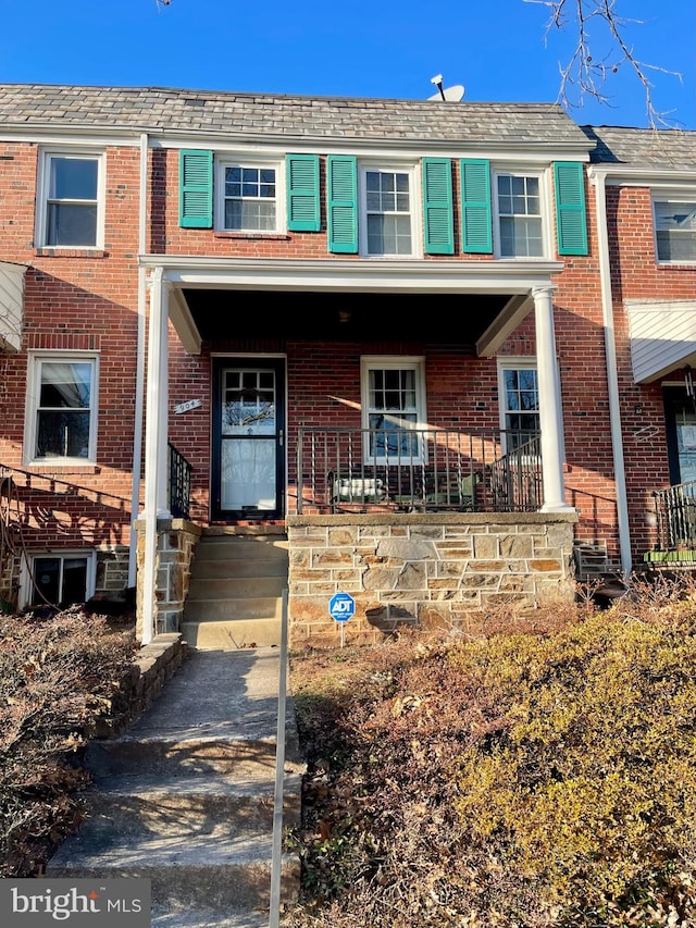 view of property with a high end roof, covered porch, and brick siding