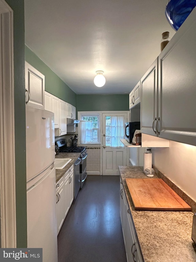 kitchen featuring freestanding refrigerator, black microwave, white cabinets, and stainless steel gas range oven