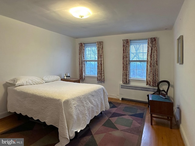 bedroom with multiple windows, radiator heating unit, wood finished floors, and baseboards