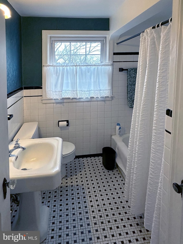 full bathroom featuring toilet, a wainscoted wall, a shower with shower curtain, a sink, and tile walls