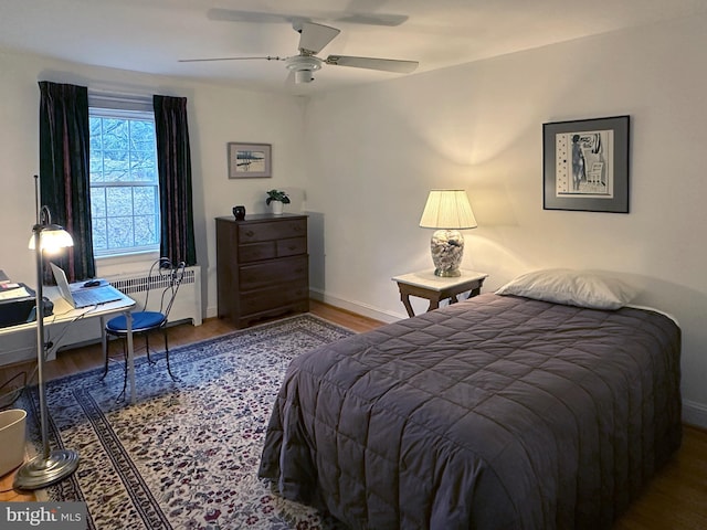 bedroom with radiator heating unit, baseboards, ceiling fan, and wood finished floors