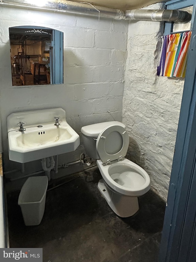 bathroom featuring concrete flooring, concrete block wall, a sink, and toilet