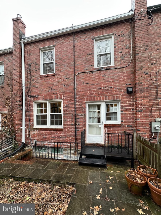 back of property with brick siding, fence, and a chimney