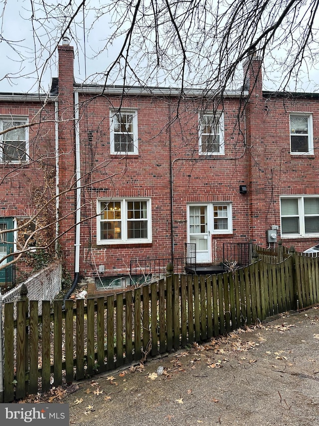 rear view of house with a fenced front yard, brick siding, and a chimney