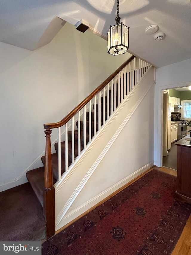 staircase featuring baseboards, wood finished floors, and a notable chandelier