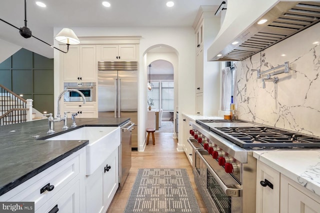 kitchen featuring arched walkways, recessed lighting, a sink, wall chimney range hood, and appliances with stainless steel finishes