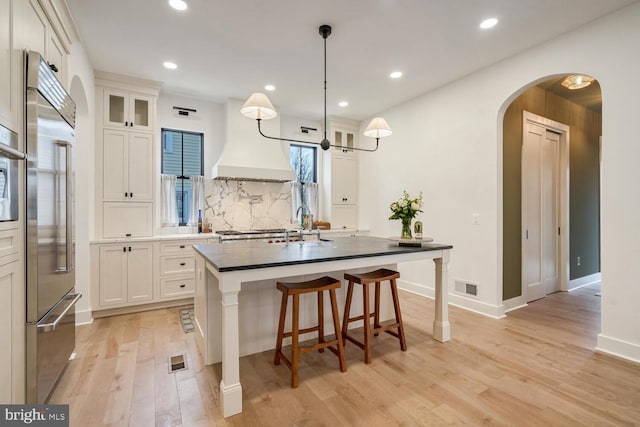 kitchen with arched walkways, light wood finished floors, custom range hood, visible vents, and stainless steel built in fridge