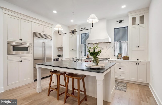 kitchen with stainless steel appliances, premium range hood, a sink, and light wood-style floors