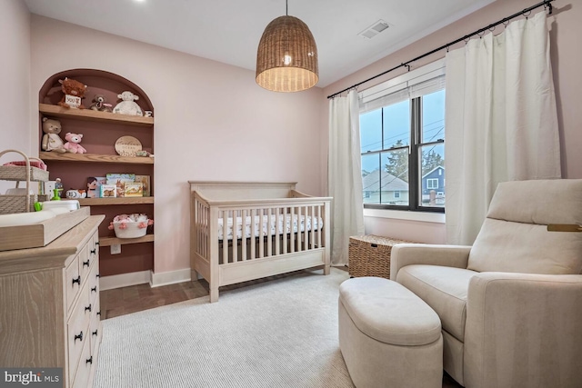 bedroom featuring a crib, carpet, visible vents, and baseboards