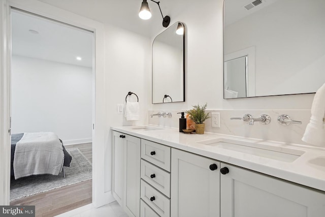 ensuite bathroom featuring double vanity, a sink, visible vents, and connected bathroom