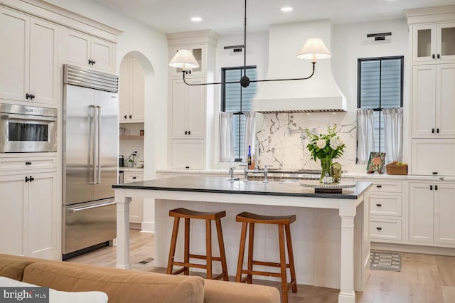 kitchen with a breakfast bar, tasteful backsplash, light wood-style flooring, appliances with stainless steel finishes, and an island with sink