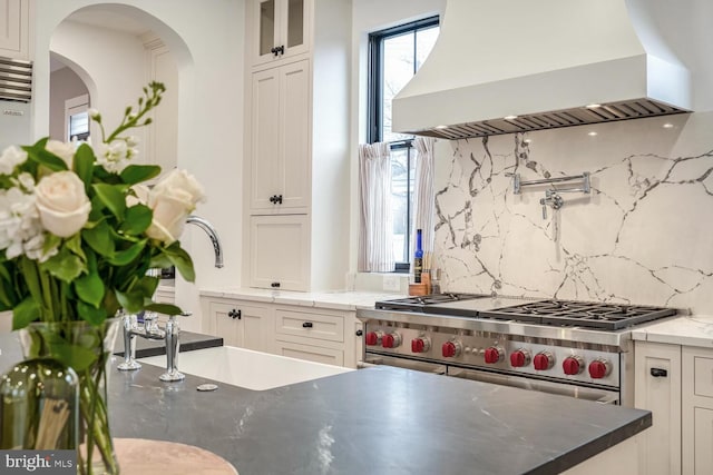 kitchen featuring tasteful backsplash, wall chimney range hood, stainless steel range, and white cabinets