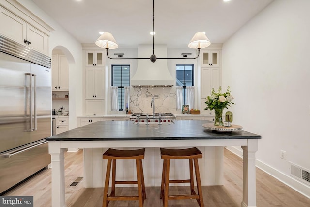 kitchen featuring light wood finished floors, visible vents, decorative backsplash, a kitchen breakfast bar, and built in refrigerator