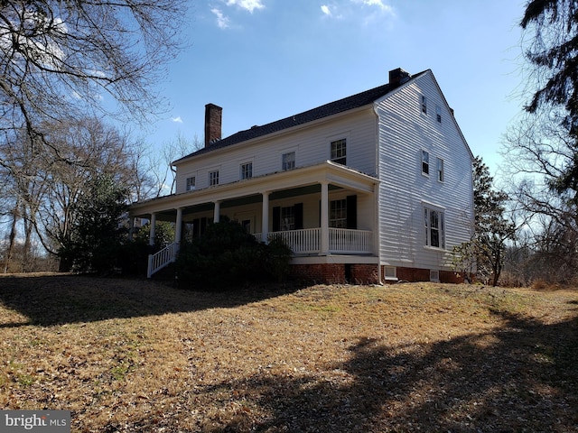 back of property with covered porch, a lawn, and a chimney
