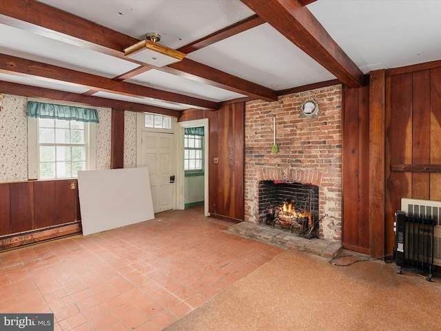 unfurnished living room featuring a brick fireplace, wood walls, beamed ceiling, and a healthy amount of sunlight