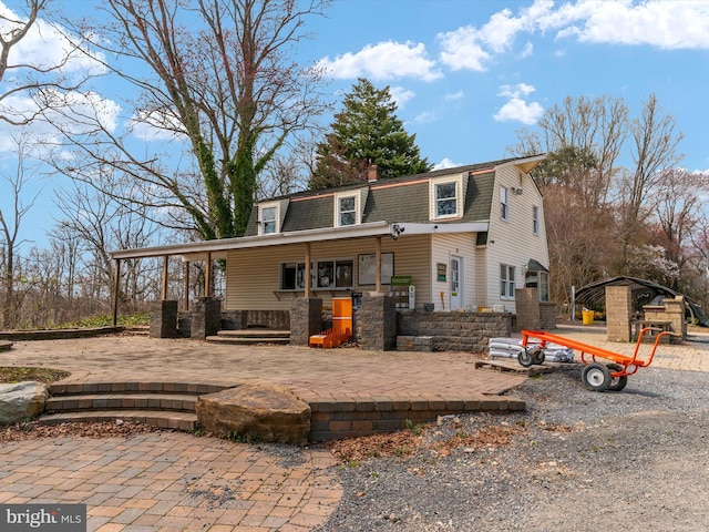 rear view of property featuring a gambrel roof and roof with shingles