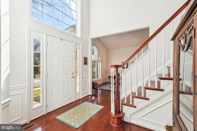 entryway featuring visible vents, dark wood-style flooring, a high ceiling, a decorative wall, and stairs