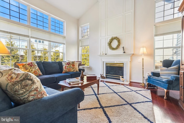 living room featuring a fireplace, wood finished floors, baseboards, and high vaulted ceiling