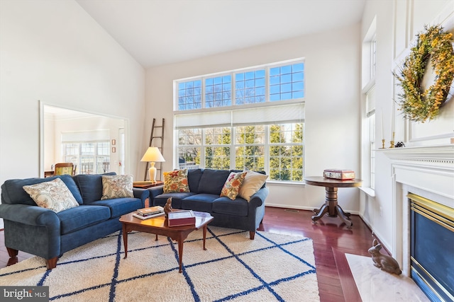 living room with a fireplace with flush hearth, high vaulted ceiling, baseboards, and wood finished floors