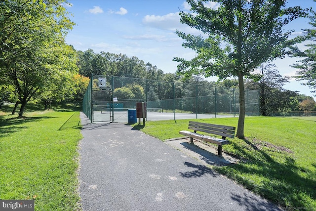 view of property's community featuring a gate, a yard, a tennis court, and fence