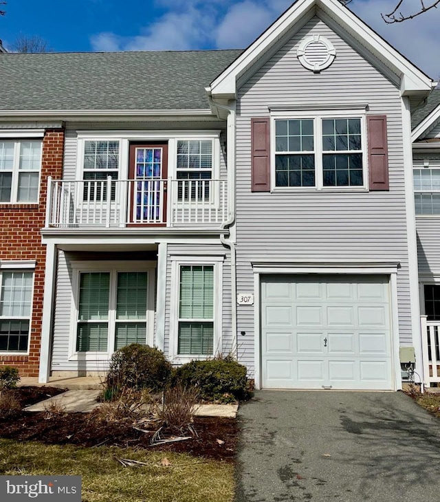 view of property with brick siding, an attached garage, roof with shingles, a balcony, and driveway