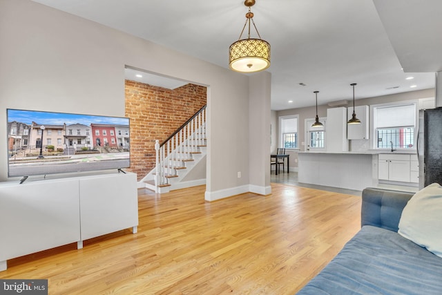 living room featuring light wood finished floors, baseboards, brick wall, stairs, and recessed lighting