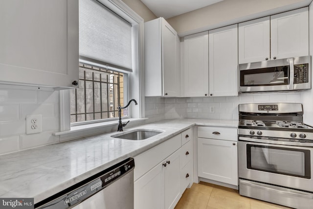 kitchen featuring backsplash, appliances with stainless steel finishes, white cabinetry, a sink, and light stone countertops